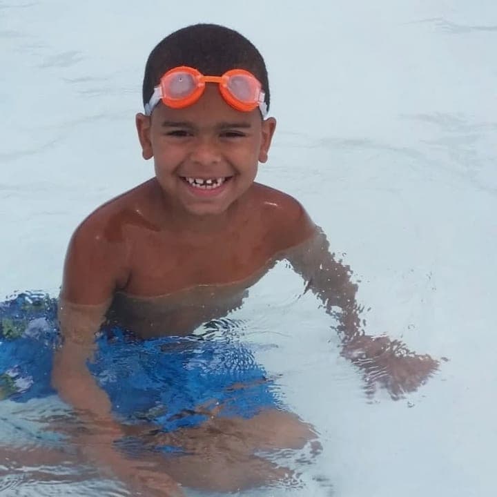 Issaka as a kid in a swimming pool, grinning in orange goggles