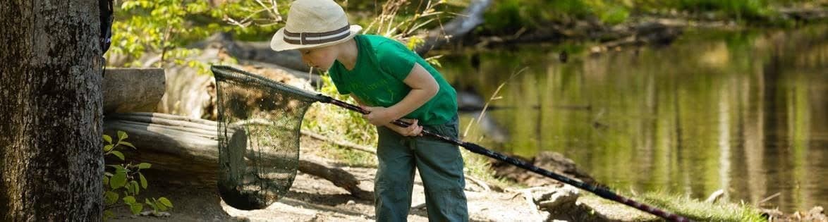 Oliver as a boy in a sun hat, dipping a long-handled net at the edge of a river