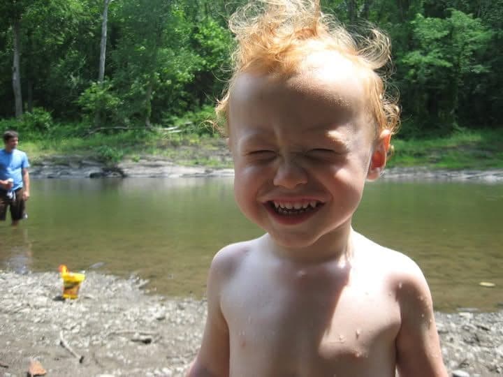 Oliver as a toddler, grinning on a riverbank