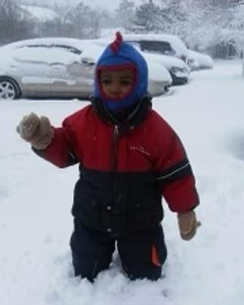 Theodore as a toddler in a red snowsuit and blue hat, standing in deep snow